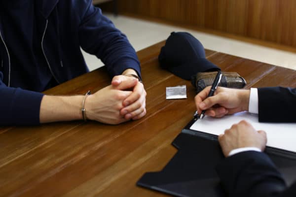 Police,Officer,Interrogating,Criminal,In,Handcuffs,At,Desk,Indoors